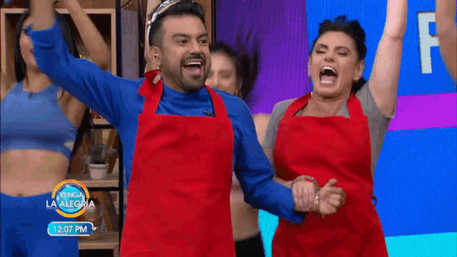 a man and a woman in red aprons are dancing in front of a sign that says 12:07 pm