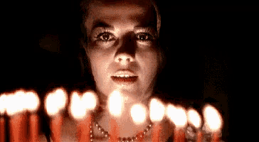 a woman is holding a bunch of lit candles in front of her face