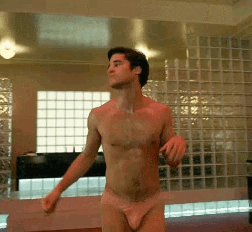a shirtless man in pink underwear is dancing in a room with a brick wall behind him .