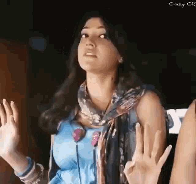 a woman in a blue dress and scarf is making a funny face with her hands in the air .