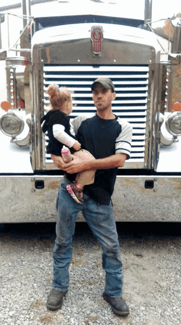 a man is holding a baby in front of a kenworth truck