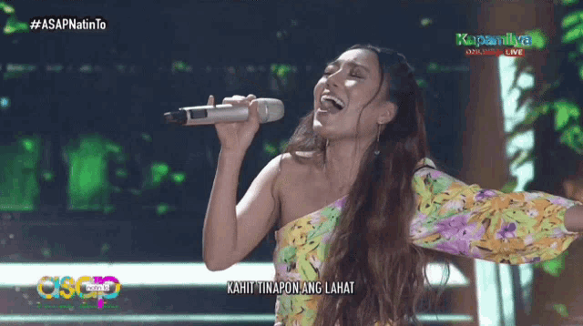 a woman singing into a microphone with the words kahit tinatapon ang lahat on the bottom