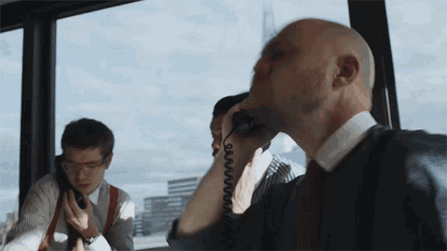 a man talking on a phone while another man sits behind him