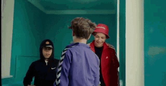 a group of young men are standing next to each other in a room . one of the men is wearing a red hat .