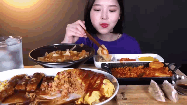 a woman in a blue shirt is eating a plate of food from a wooden table