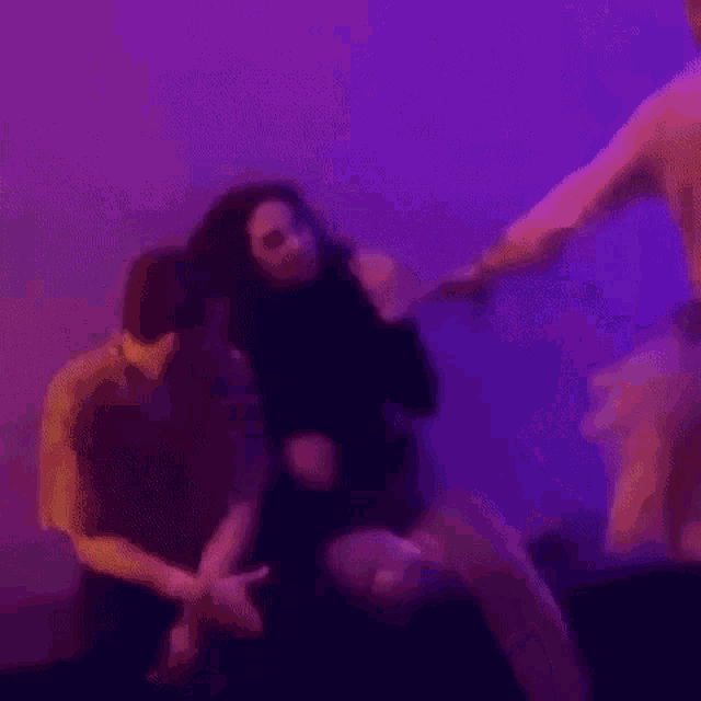 a group of people are sitting in a room with purple lights and talking to each other .