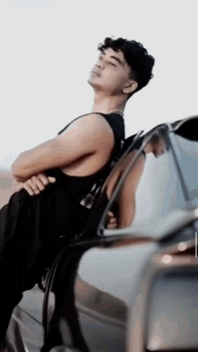 a young man leaning against a car with his arms crossed