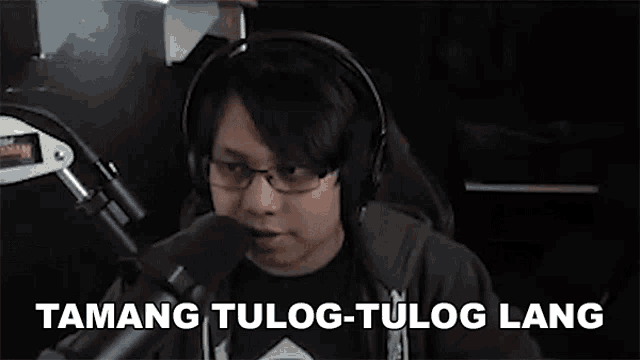 a young man wearing headphones and glasses is talking into a microphone .