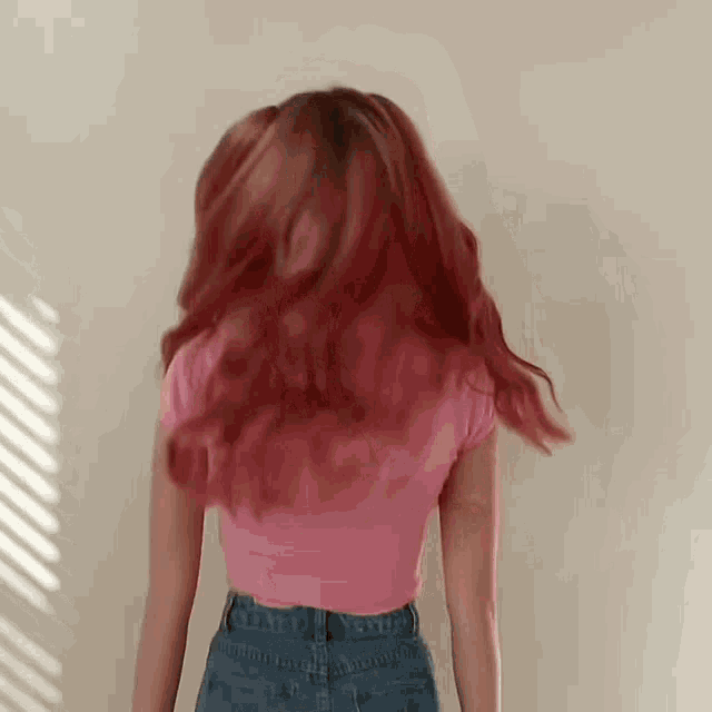 a woman with red hair is wearing a pink top and blue jeans