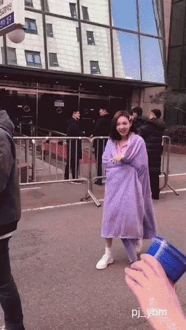 a woman in a purple coat is standing in front of a building with pj_ybm written on the bottom