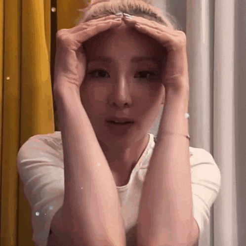 a woman is holding her hands on her forehead and looking at the camera .