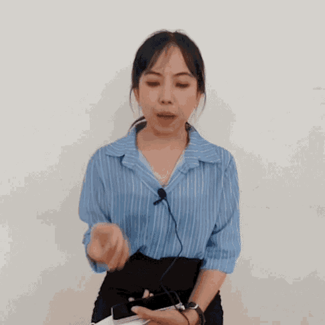 a woman wearing a blue striped shirt and a microphone is holding a cell phone in her hand .