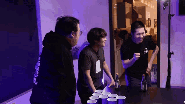 a man wearing a black shirt with the word signal on the back is playing beer pong