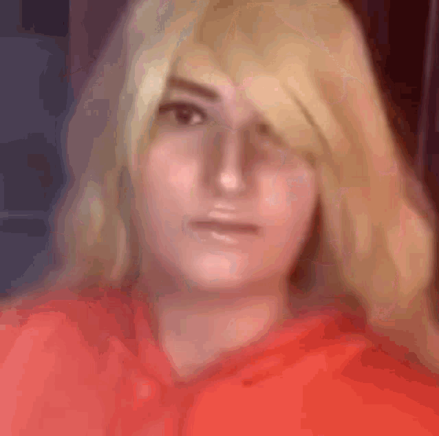 a woman with blonde hair and a red hoodie is looking at the camera .