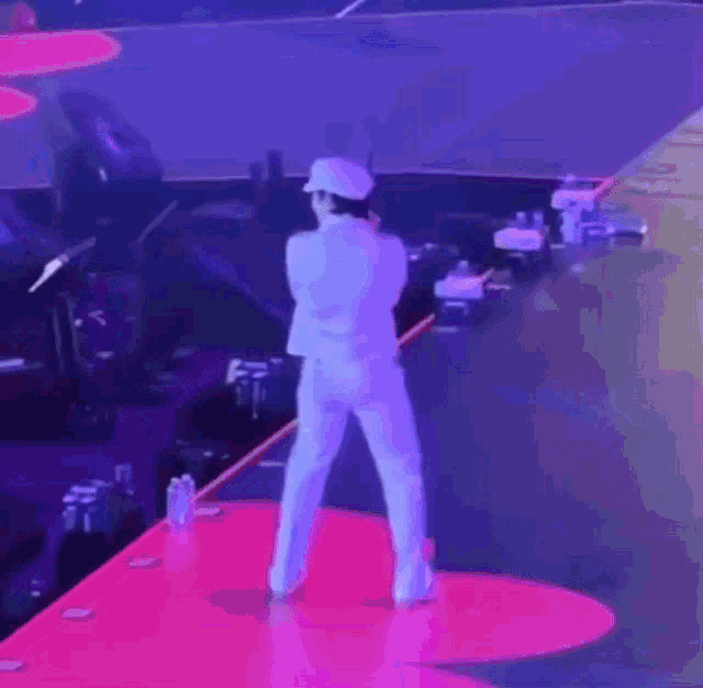 a man in a white suit and hat is standing on a stage .