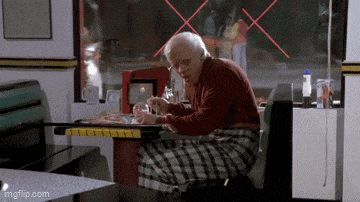 an elderly man is sitting at a table in a diner eating a hamburger .