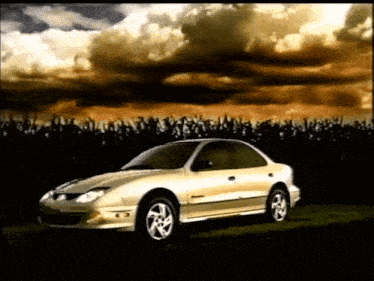 a silver car is parked in a field with a cloudy sky behind it
