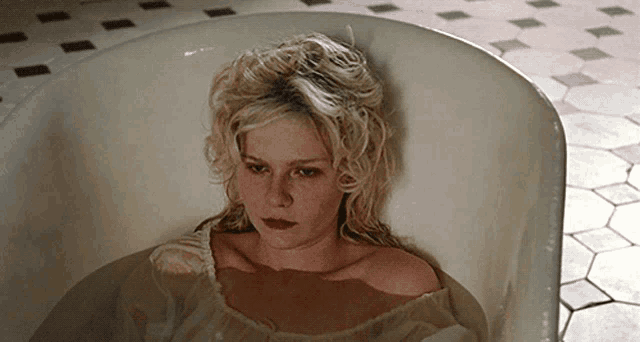 a woman is laying in a bathtub with a tiled floor behind her