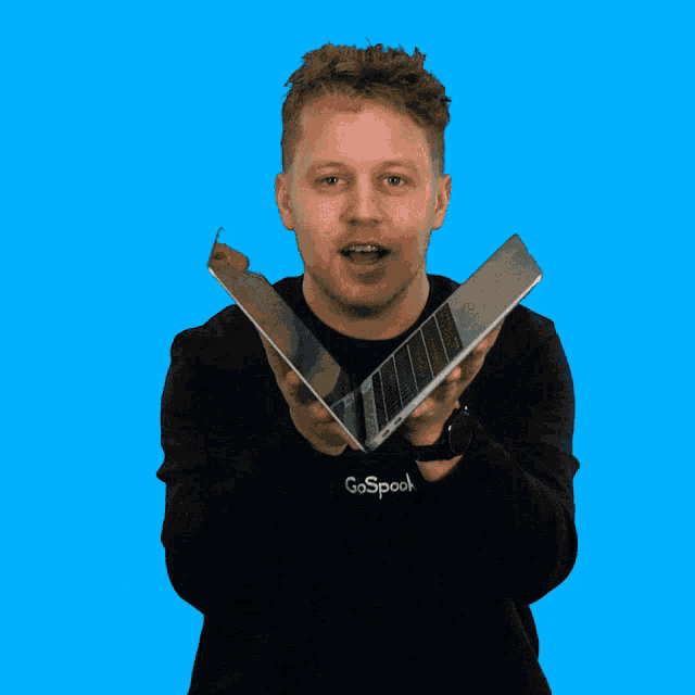 a man wearing a go spooky sweatshirt holds a laptop and a tablet