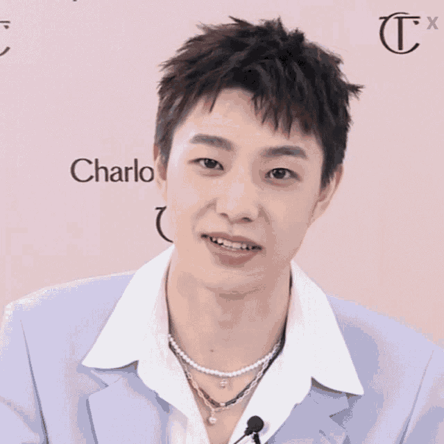 a young man wearing a purple jacket and a pearl necklace stands in front of a wall that says charlo
