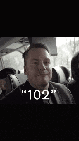 a man in a suit is sitting in a bus with the number 102 on his face