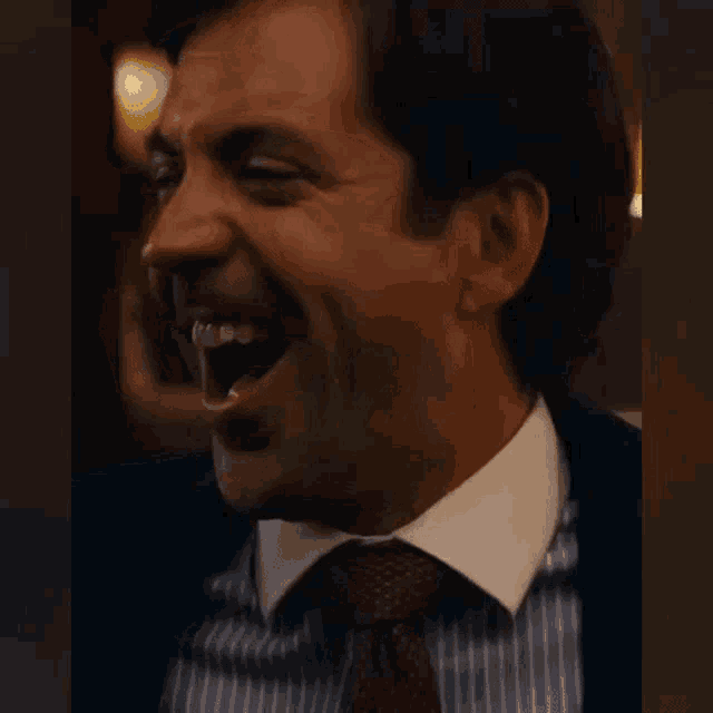 a man in a suit and tie is laughing with his eyes closed .