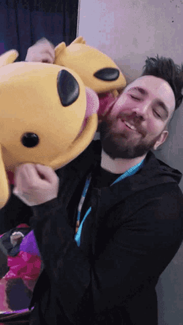 a man with a beard is hugging a stuffed animal with a pink tongue