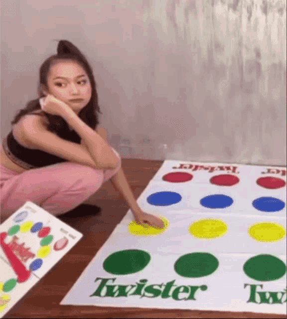 a woman is squatting down next to a twister game on the floor .