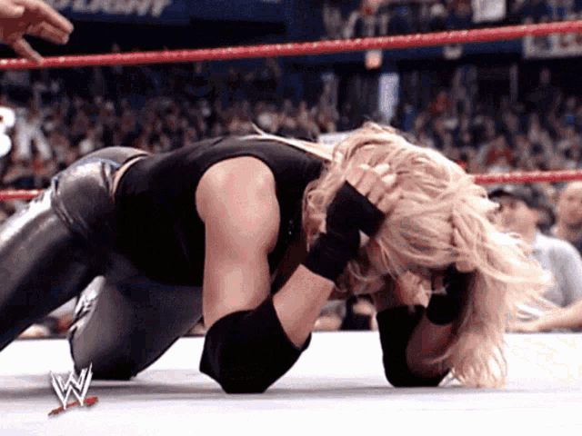 a woman is kneeling down in a wrestling ring with a w logo on the bottom