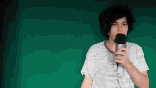 a young man is singing into a microphone while wearing headphones .