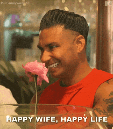 a man in a red shirt is smelling a pink flower and the caption says happy wife happy life