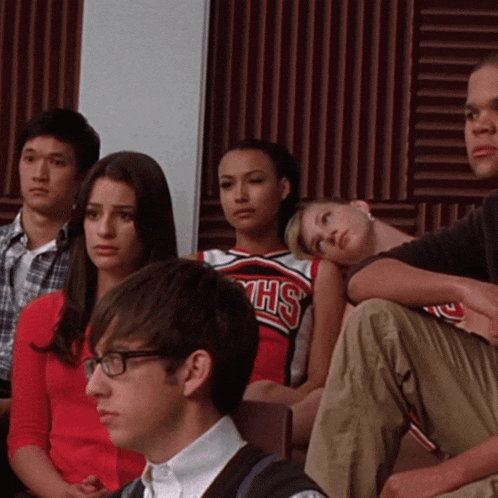 a group of people are sitting in a room and one of the girls is wearing a cheerleader uniform that says shs