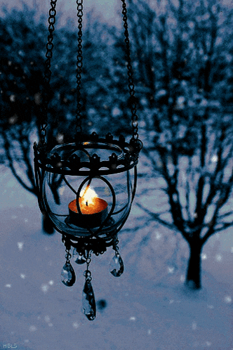 a candle in a glass hanging from a chain with hbls written below it