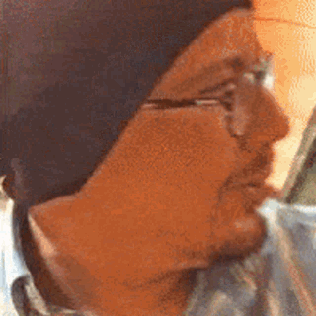 a man wearing glasses and a beanie is drinking from a glass