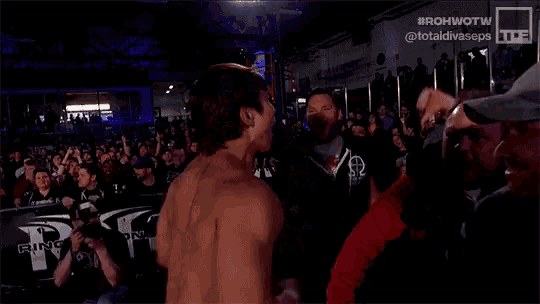 a man without a shirt is shaking hands with another man in a wrestling ring .
