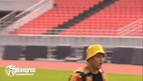 a man wearing a yellow hat is walking on a track in front of a stadium .