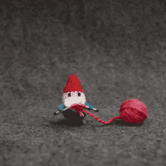 a crocheted gnome is pulling a ball of red yarn