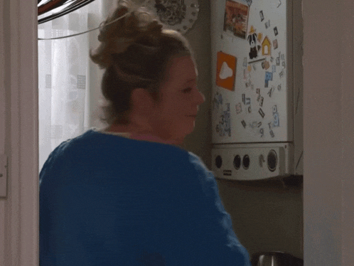 a woman stands in front of a fridge that has stickers on it including one that says ' a ' on it