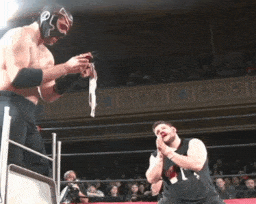a man in a black shirt with the number 1 on it stands in a wrestling ring