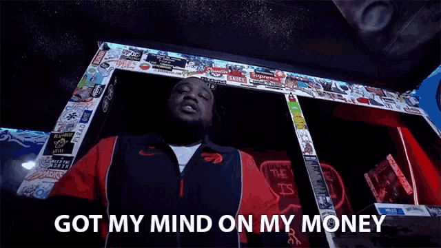 a man in a red and black jacket is standing in front of a sign that says got my mind on my money