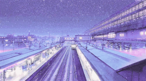 a train station with snow falling on the tracks and a building in the background