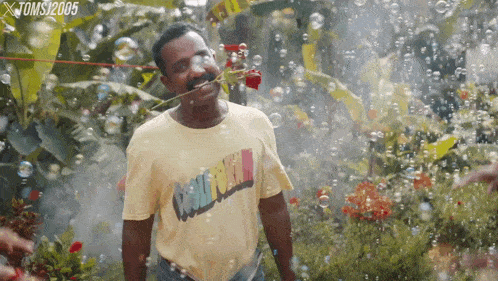 a man wearing a yellow t-shirt that says cool crew holds a rose in his mouth
