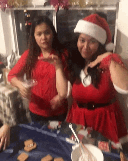 two women wearing santa hats are standing next to each other at a table