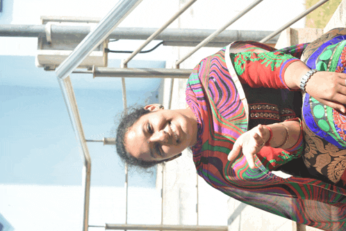 a woman wearing a colorful dress is sitting on a ledge