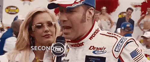 a man in a race car is talking into a microphone next to a woman in sunglasses .