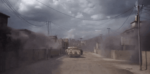 a military vehicle driving down a dirt road with a cloudy sky in the background