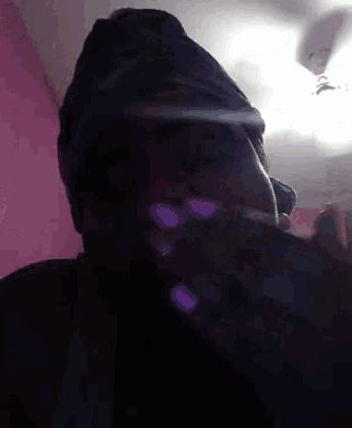 a person wearing a hat is smoking a cigarette in a dark room