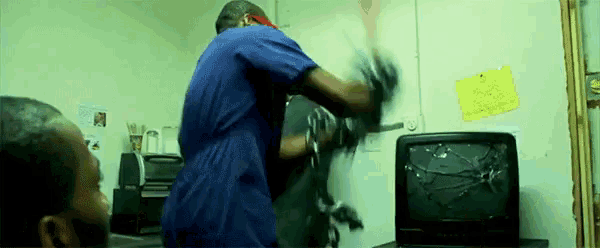 a man in a blue shirt is standing next to a broken television