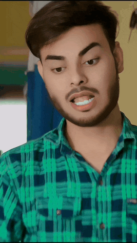 a man with a beard is wearing a green plaid shirt and making a funny face