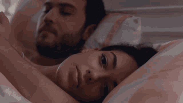 a man and woman are laying in bed and the woman is looking at the camera